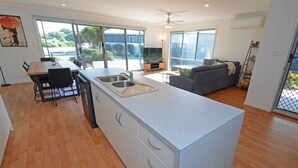 A modern kitchen with a large island, dining area, and a living space with a sofa and TV.