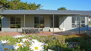 A modern single-story building with a covered patio area, large windows, and a small outdoor seating area.