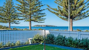 A coastal garden with a white fence, a birdbath, and a view of the sea and a distant island. - Saltys—Oceanfront Retreat near Dining & Bay Walks (Victor Harbor)
