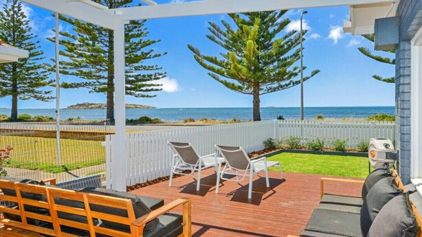 A covered outdoor area with wooden deck, white chairs, and a grill. - Saltys—Oceanfront Retreat near Dining & Bay Walks (Victor Harbor)