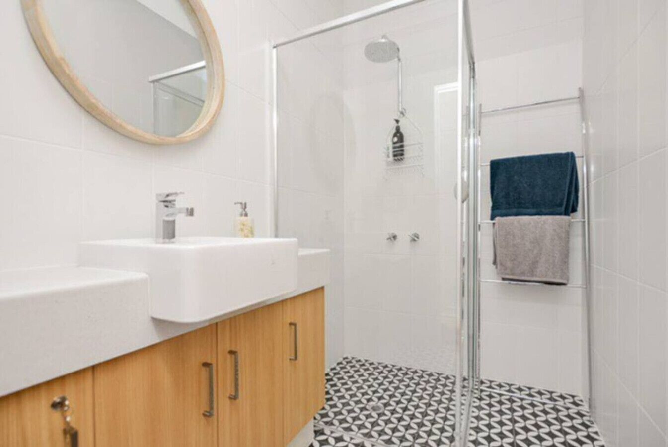 Une salle de bain moderne avec une douche, deux lavabos, un miroir et un revêtement de sol à motifs.