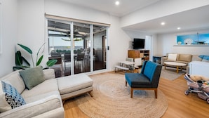 A spacious living area with a sliding glass door leading to a balcony, a sofa, a blue armchair, a small table, and a television. - Saltys—Oceanfront Retreat near Dining & Bay Walks (Victor Harbor)