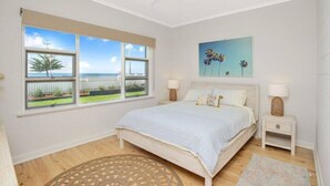 A bedroom with a bed, two bedside tables, a ceiling fan, and a large window with a view of the outdoors. - Saltys—Oceanfront Retreat near Dining & Bay Walks (Victor Harbor)