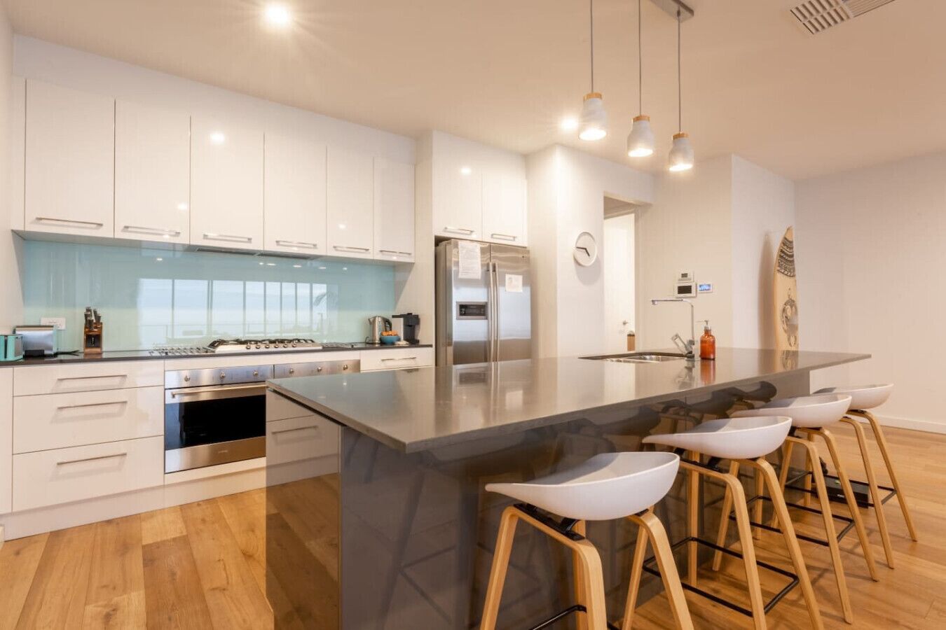 A modern kitchen with white cabinets, a large island with stools, stainless steel appliances, and pendant lighting.