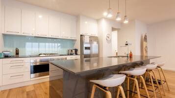 A modern kitchen with white cabinets, a large island with stools, stainless steel appliances, and pendant lighting.