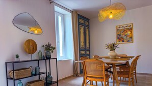 A dining area with a round table, wicker chairs, a black metal shelf with baskets, and a mirror. - La Gloriette en Luberon 15 minutes from GORDES (Goult)