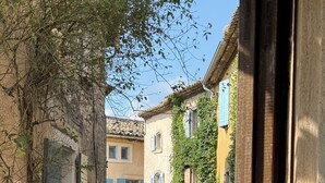 A narrow street with buildings on either side, some with vines and shutters, and a parked car in the distance. - La Gloriette en Luberon 15 minutes from GORDES (Goult)