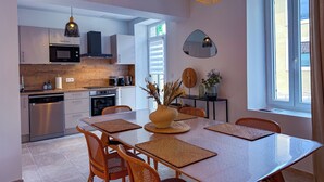 A modern kitchen with stainless steel appliances, a dining area with a large table and woven placemats, and a unique ceiling light fixture. - La Gloriette en Luberon 15 minutes from GORDES (Goult)