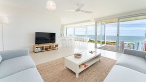 Una sala moderna con un televisor de pantalla plana, una mesa de centro y dos sofás. Una ventana grande ofrece vistas al océano.