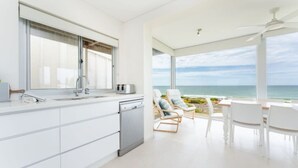 Una cocina moderna con vista al océano, un comedor con sillas blancas y un ventilador de techo.