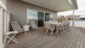 Un patio exterior con una terraza de madera, una mesa con sillas y dos sillones a rayas.