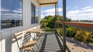 Un balcon avec une table et des chaises en bois, une rambarde en métal et une vue sur la verdure et les arbres.