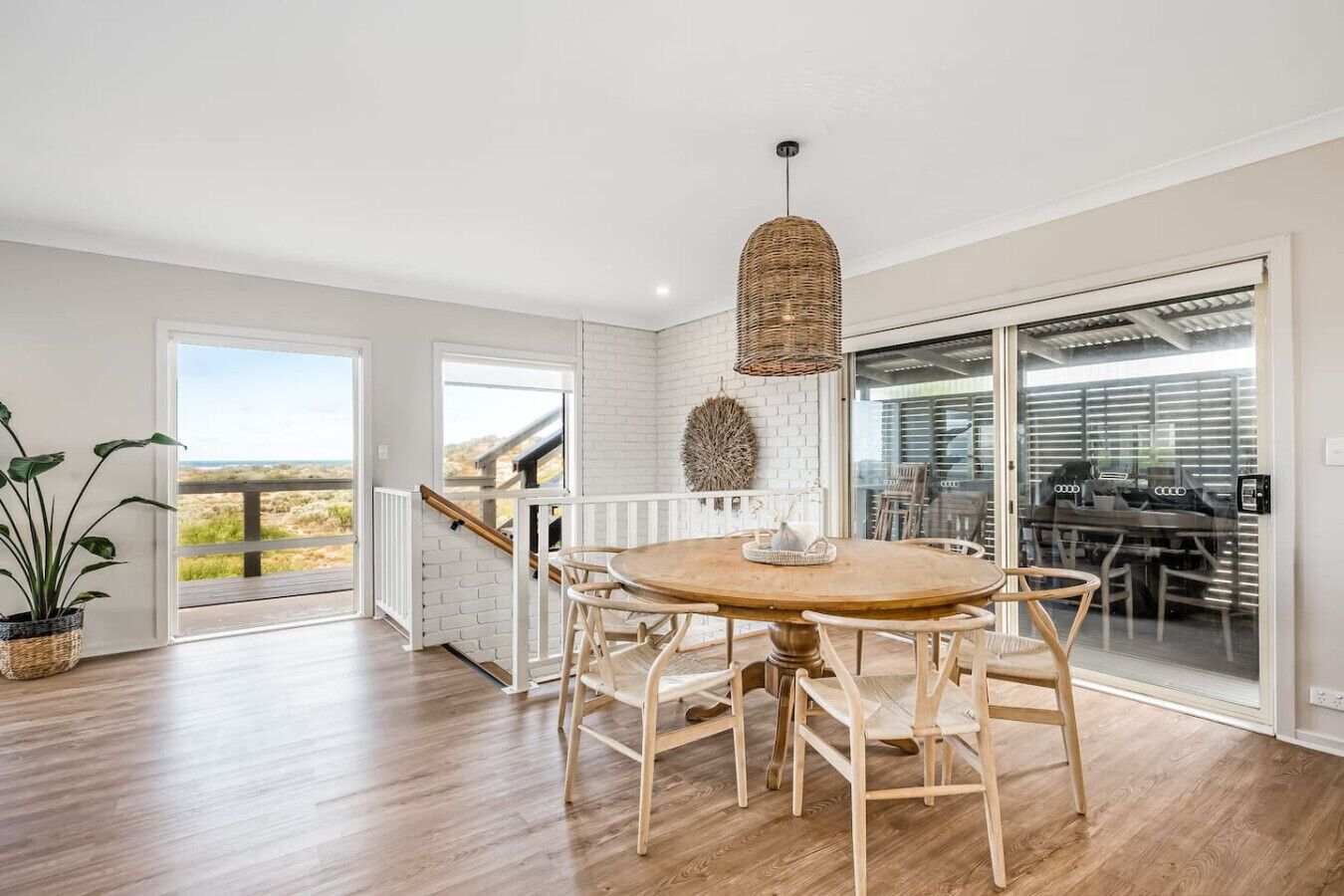 A spacious dining area with a round wooden table and chairs, a hanging light fixture, and a view of the outdoors through large sliding glass doors.