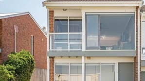 Un immeuble résidentiel de deux étages doté d’un balcon, de grandes fenêtres et d’une façade en briques.