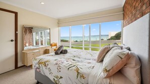 Une chambre avec un grand lit, une commode, un miroir et une vue sur la mer.