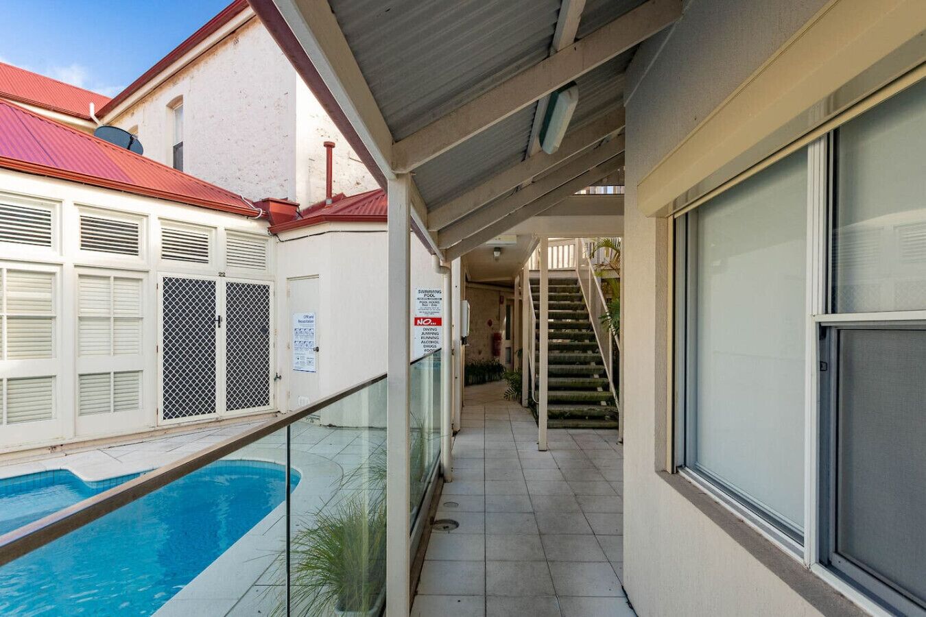 Un espacio al aire libre cubierto con una piscina, una escalera y un edificio con techo rojo.