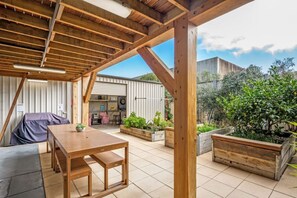 Une terrasse extérieure avec des meubles en bois, un espace salon couvert et des jardinières agrémentées de plantes.