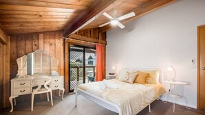 A bedroom with a bed, bedside table, and a dresser. There is a window with curtains and a view of the outside.