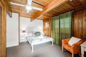 Une chambre à coucher avec un lit, une table de chevet, une chaise, un ventilateur de plafond et des murs en bois.