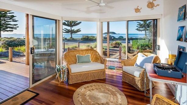 A spacious room with a large sliding glass door leading to a balcony with a view of the ocean. There are two wicker sofas and a small table with a laptop.