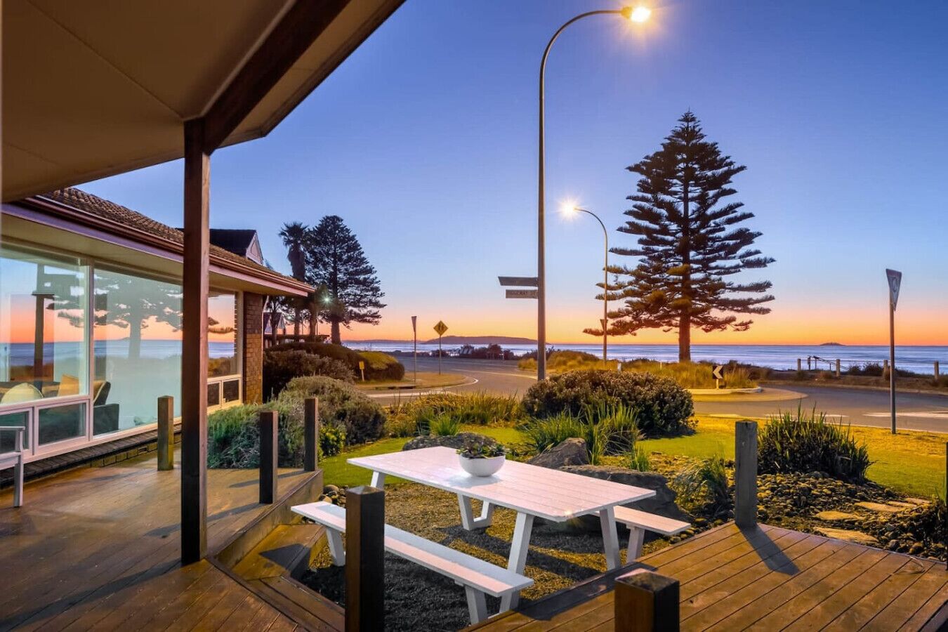 A modern house with a patio overlooking a coastal road.
