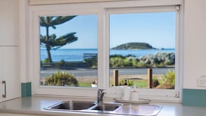 A kitchen with a double sink and a window overlooking a beach and ocean.