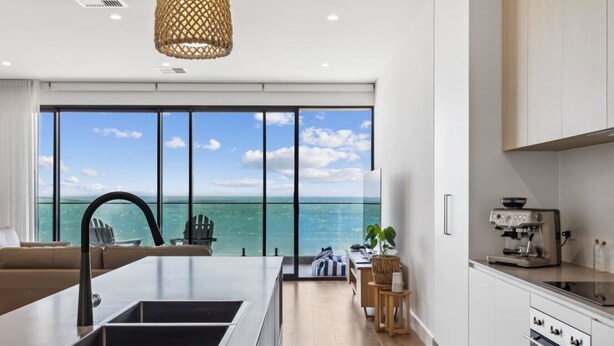 A modern kitchen with a large island, a coffee machine, and a view of the ocean. - Seamist on Seagull with Expansive Views (Hayborough)