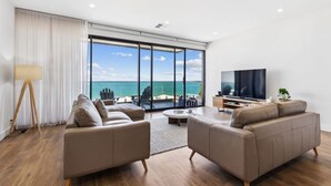 A modern living room with a large TV, comfortable seating, and a view of the ocean. - Seamist on Seagull with Expansive Views (Hayborough)