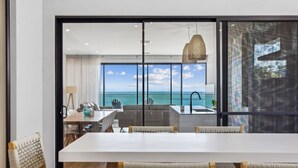 A modern kitchen with a large island, a dining area with wicker chairs, and a view of the ocean. - Seamist on Seagull with Expansive Views (Hayborough)