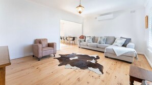 Un salón espacioso con un sofá de color claro, un sillón de cuero y un tapiz de cuero de vaca.