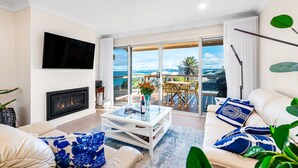 A modern living room with a fireplace, a flat-screen TV, a glass coffee table, and a sofa with blue cushions.