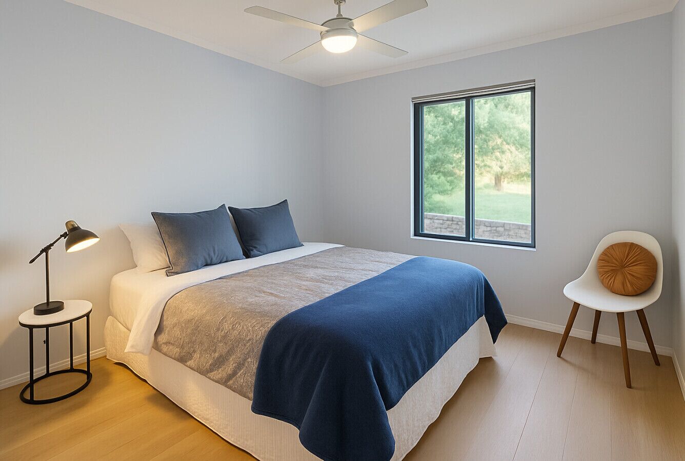 Ein Schlafzimmer mit einem Bett, einem Nachttisch, einem Sessel, einem Fenster und einem Deckenventilator.