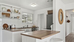 A modern kitchen with white cabinetry, a wooden countertop, and a breakfast bar with two stools. - Percy`s Place: Family-friendly Waterfront Serenity (Goolwa)