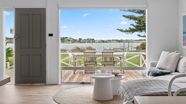 A room with a large sliding glass door leading to an outdoor deck with a view of a lake and houses. - Percy`s Place: Family-friendly Waterfront Serenity (Goolwa)