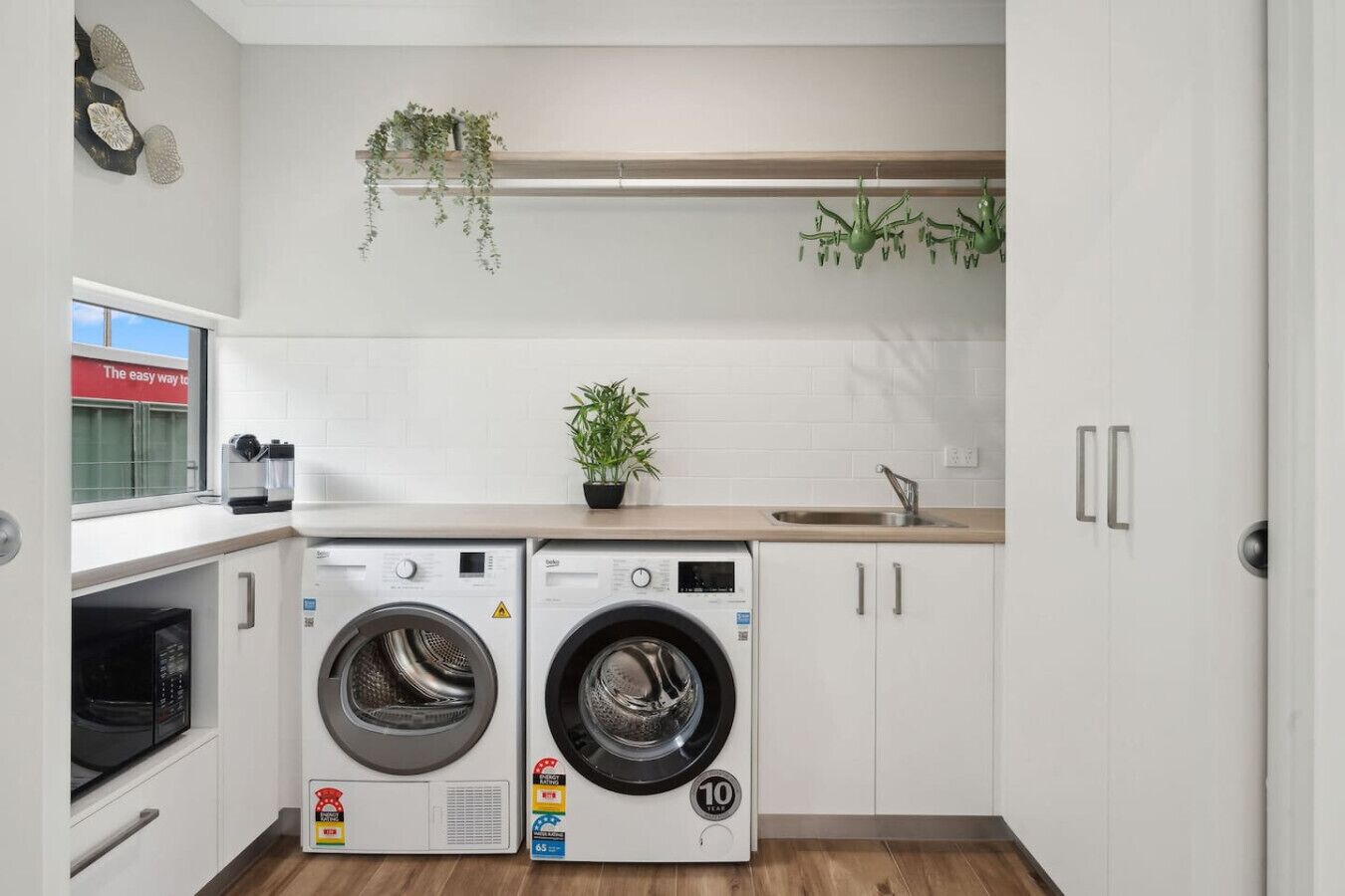 A compact laundry room with two front-loading washing machines, a microwave, and a sink.
