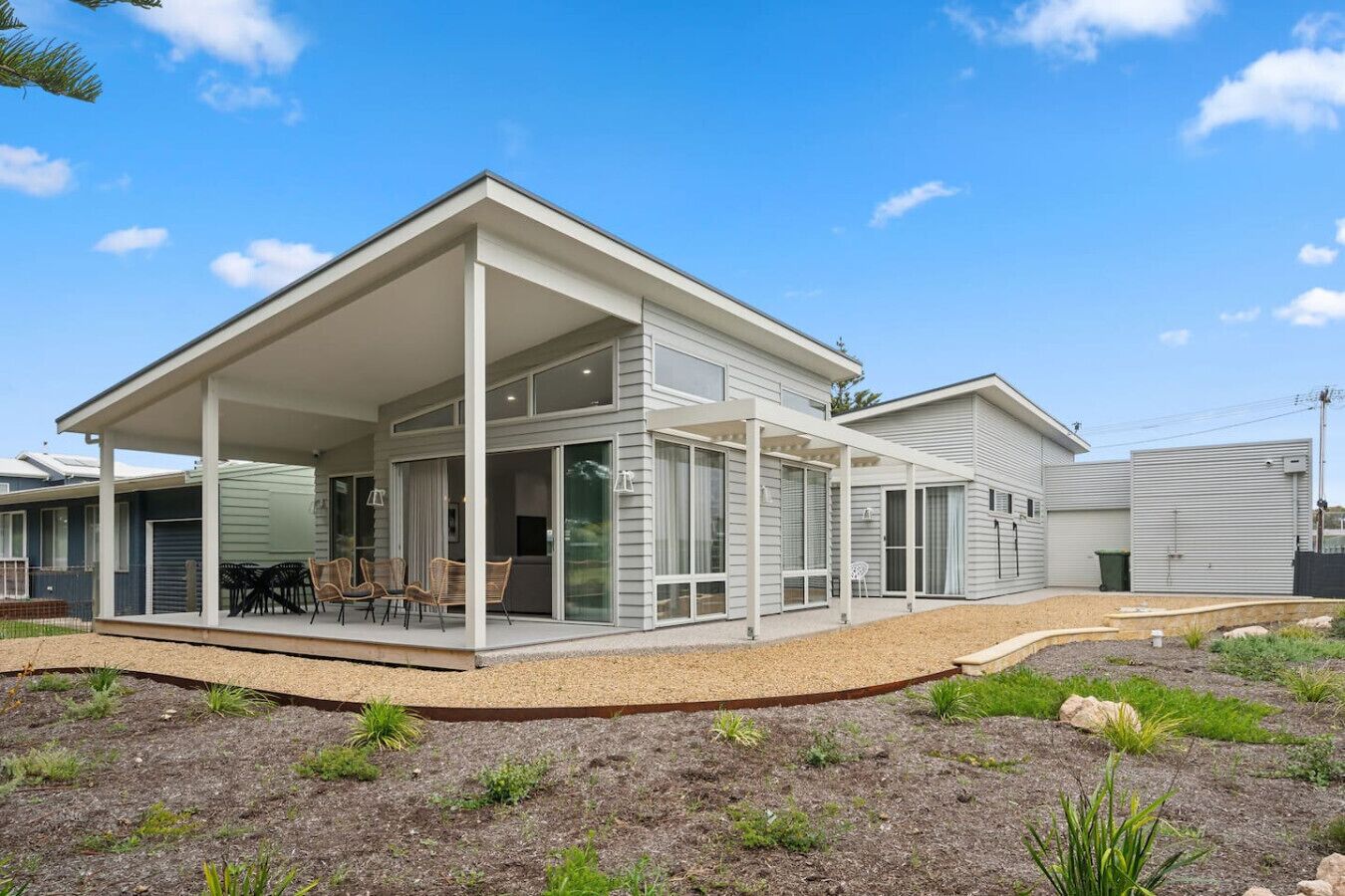 Une maison moderne à deux étages, dotée d’un patio couvert, de grandes fenêtres et d’un jardin bien entretenu.