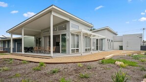 A modern two-story house with a covered patio, large windows, and a well-maintained garden.