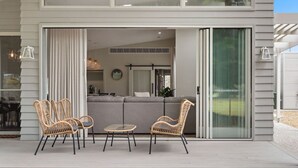 A modern house with a patio area featuring wicker furniture and a sliding glass door leading to an interior with a gray sofa and a kitchen.