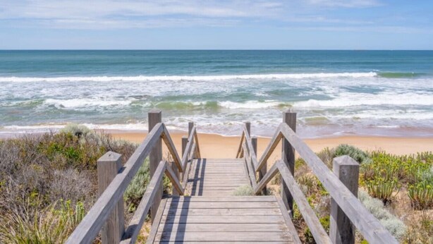 Un muelle de madera que conduce a una playa, con olas al fondo.