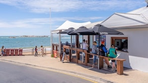 Un café costero con terraza, vistas al mar y un edificio blanco con tejado inclinado.