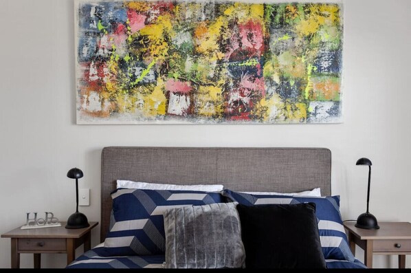 Un dormitorio con una cama, dos mesitas de noche y un cuadro abstracto de colores en la pared.
