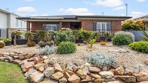 Una casa de dos pisos con fachada de ladrillo, un porche delantero y un jardín ajardinado con diversas plantas y un borde de piedras.