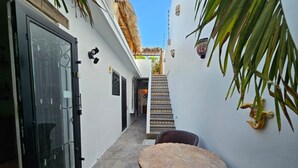 Un callejón estrecho con una puerta, una escalera y una mesa redonda con sillas.