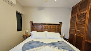 Una cama bien hecha con cabecera de madera, una mesita de noche con lámpara y un armario con puertas empañadas.