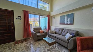 A living room with a stone floor, a sofa, a chair, a small table, and a door. - Pool, Park & Ocean - Centro Home (Mazatlan)