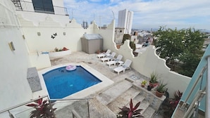 A rooftop pool area with lounge chairs, potted plants, and a view of the cityscape. - Pool, Park & Ocean - Centro Home (Mazatlan)
