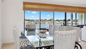 Una habitación moderna con una mesa de vidrio, sillas de mimbre y vistas a un puerto deportivo.