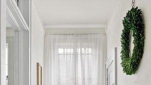 Un pasillo con una puerta blanca, una silla verde, una mesita con una planta y un tapete estampado.