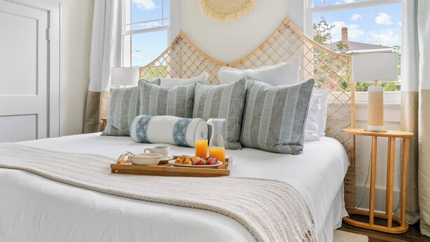 Una cama bien tendida con una bandeja de alimentos para el desayuno, un tapiz tejido y vistas del cielo a través de amplias ventanas.