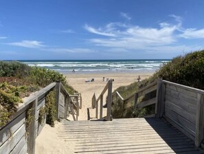 En trætrap der fører ned til en strand med kig til havet og sand.